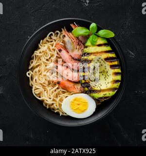 Cuisine asiatique. Nouilles aux crevettes, aux avocats, aux œufs et aux graines de chia. Sur fond de pierre noire. Vue de dessus. Espace de copie disponible. Banque D'Images