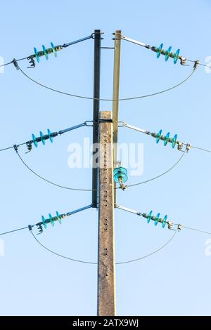 Détail d'un pôle d'alimentation électrique avec trois câbles de distribution d'électricité contre un ciel bleu. Banque D'Images