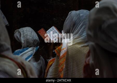 Lalibela, Ethiopie - Nov 2018: Les femmes vêtues de blanc traditionnel, assis au crépuscule et lire livre de prières à côté des églises souterraines de la Banque D'Images
