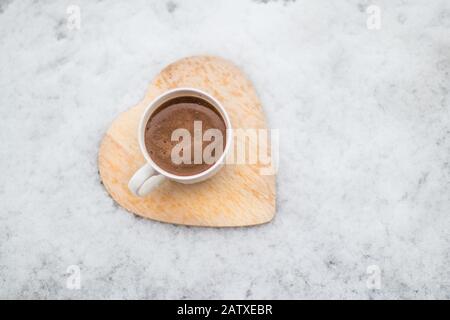 Du café sur un dessous de verre en bois dans la neige en hiver. Banque D'Images