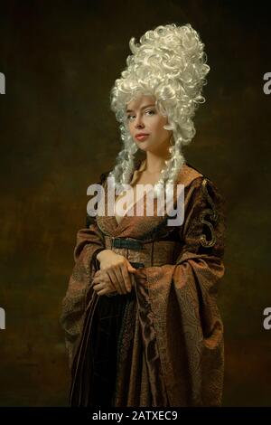 Portrait de la jeune femme médiévale dans des vêtements brun vintage debout sur fond sombre. Femme modèle comme duchesse, personne royale. Concept de comparaison des époques, moderne, de la mode, de la beauté. Banque D'Images