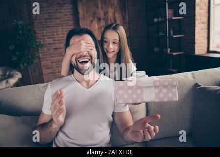 Photo d'une petite adorable jolie dame qui cachait les yeux son beau jeune papa s'asseoir confortable canapé tenant une grande surprise giftbox anniversaire présent domestique Banque D'Images