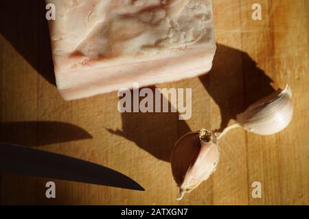 Le grand morceau de lard, un couteau et deux gousses d'ail se trouvent sur la table Banque D'Images