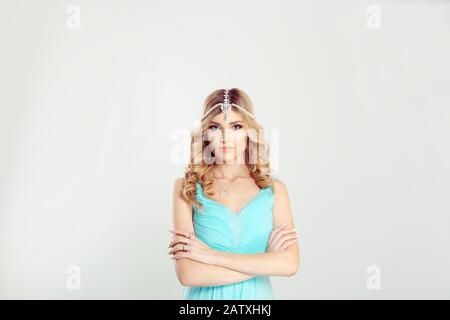 Femme grincheux. Femme cheveux blond curly dans tikka bijoux orientaux sur les bras de tête croisé en regardant vous frustré isolé blanc gris mur de fond Banque D'Images