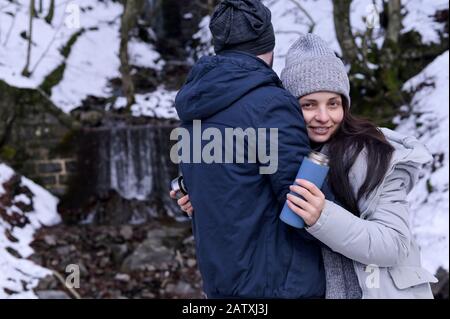 Une jeune femme et un homme qui s'émiettent dans une forêt enneigée. Une paire d'amoureux en vêtements d'hiver. La fille tient un thermos dans ses mains. Espace de copie Banque D'Images