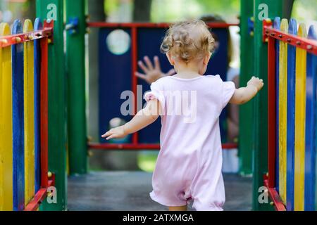 Une jolie fille joue sur le terrain de jeux. L'enfant d'un an va à la mère. Banque D'Images