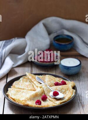 Crêpes servies avec de la crème aigre, des framboises et du miel. Le plat traditionnel de Carnaval et de Maslenitsa. Banque D'Images