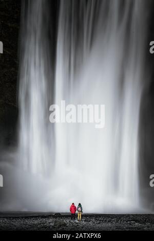 Deux touristes se trouvent devant la cascade massive de Skogafoss sur la coust sud de l'Islande Banque D'Images