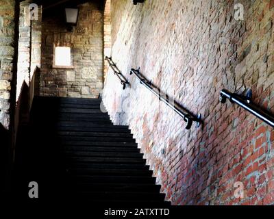 Escalier extérieur en béton dans la brique couverte et mur de château en pierre avec mur de briques texturées d'un côté et vieux rambarde d'acier noir de style ancien. Banque D'Images