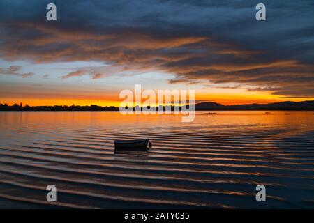 Petit bateau doucement flou qui bascule dans l'eau ondulée de la baie au lever du soleil sous le ciel dramatique et les collines lointaines en arrière-plan à Tauranga, Nouvelle-Zélande. Banque D'Images