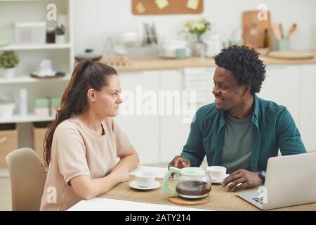 Jeune couple assis à la table et s'entretenir l'un avec l'autre tout en prenant le petit déjeuner ensemble dans la cuisine Banque D'Images