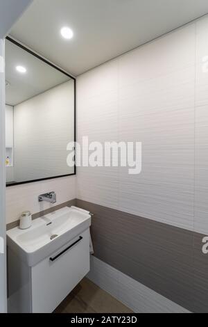 nouvel intérieur moderne de toilettes aux couleurs claires avec murs et carreaux de sol beige et marron. Évier blanc sur le placard. À côté - une serviette pendante, au-dessus de moi Banque D'Images