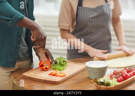 Gros plan de jeune couple debout à la table de cuisine et la cuisine ensemble l'homme coupe des légumes et femme fait de la pâte Banque D'Images