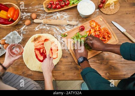 Gros plan de couple préparant la pâte et couper les légumes pour la pizza ensemble à la table de cuisine en bois Banque D'Images