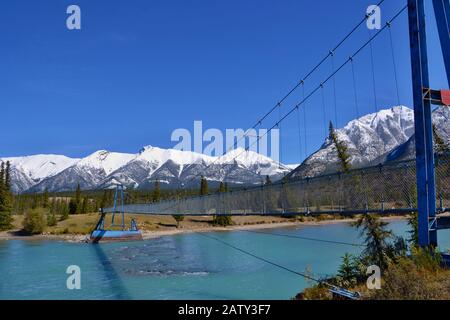 Pont suspendu bleu sur la rivière turquoise. Hautes montagnes couvertes de neige, ciel bleu, jour ensoleillé. Réserve Écologique Des Plaines Kootenay, Canada. Banque D'Images