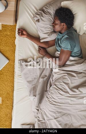 Vue à grand angle du jeune homme africain fatigué de la dure journée il dormait dans son lit dans la chambre Banque D'Images