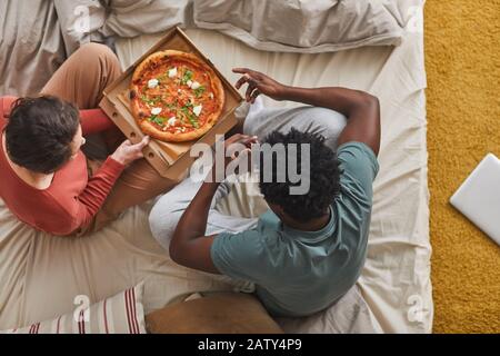 Vue sur le grand angle des jeunes couples assis sur le lit et manger de la pizza ensemble dans la chambre Banque D'Images