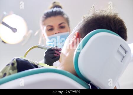 Dentiste féminin traitant les dents au patient, jeune homme en chaise à la clinique dentaire. Dentisterie, dents saines, médecine et concept de santé Banque D'Images