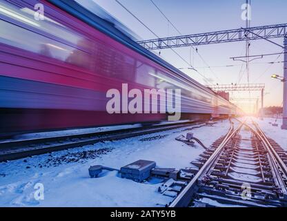 Le train à grande vitesse traverse rapidement la gare au coucher du soleil en hiver. Banque D'Images