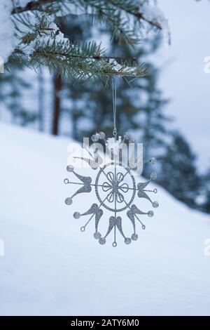 L'ornement en forme de flocon de neige se trouve sur la branche enneigée d'un arbre vert Banque D'Images