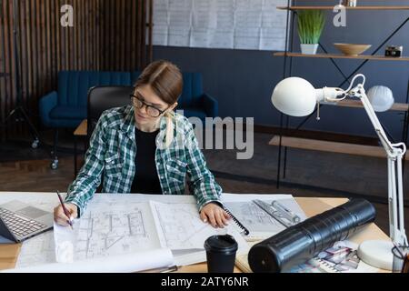 Concevoir des plans de travail au bureau. Concevoir un projet de construction par un ingénieur. Plan architectural. Gros plan portrait de belle femme de la concentricité Banque D'Images