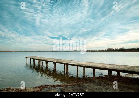 Un long pont en bois sur l'eau et le paysage nuageux Banque D'Images