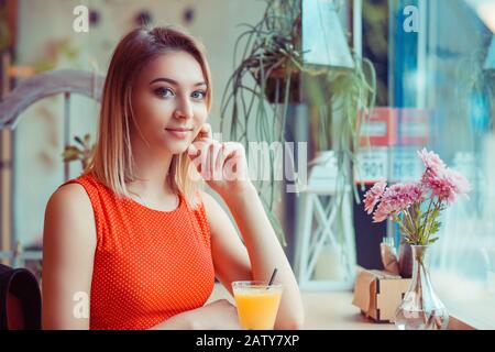 Bonne fille prenant le petit déjeuner avec jus d'orange dans le café à la maison près de la fenêtre et regardant l'appareil photo Banque D'Images