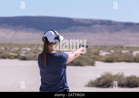 Femme en t-shirt bleu et casquette de baseball blanche pratiquant le tir ciblé à partir d'un pistolet 22 LR. Banque D'Images