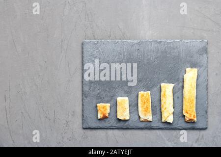 Les crêpes au fromage cottage sur une ardoise grise sont disposées sous la forme d'une tendance croissante sur un fond en béton sombre. Banque D'Images