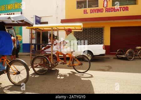 Pédicab (vélo taxi) dans une rue coloniale à Hunucma, Yucatan, Mexique. Les drapeaux de Papel Picado volent en hauteur. Banque D'Images