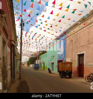Pédicab (vélo taxi) dans une rue coloniale à Hunucma, Yucatan, Mexique. Les drapeaux de Papel Picado volent en hauteur. Banque D'Images