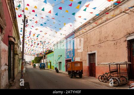 Pédicab (vélo taxi) dans une rue coloniale à Hunucma, Yucatan, Mexique. Les drapeaux de Papel Picado volent en hauteur. Banque D'Images