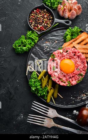 Tartare de boeuf avec jaune d'oeuf cru, concombre mariné et oignons. Cuisine française. Vue de dessus. Espace libre pour votre texte. Banque D'Images