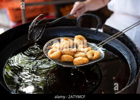 Cuisinier tient une portion de beignets fraîchement cuits sur le tamis, juste levé de l'huile. Délicieux Fast-food dans un festival en plein air Banque D'Images