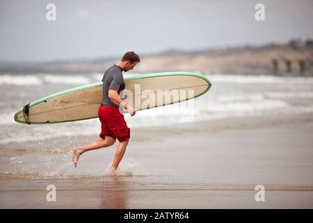 L'homme qui s'est défait de l'eau avec son planche de surf. Banque D'Images