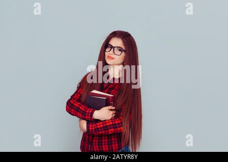 Un étudiant souriant portant une pile de livres. Femme avec des cheveux de brunette très longs et des livres en chemise carrée noire rouge sur fond gris clair Banque D'Images