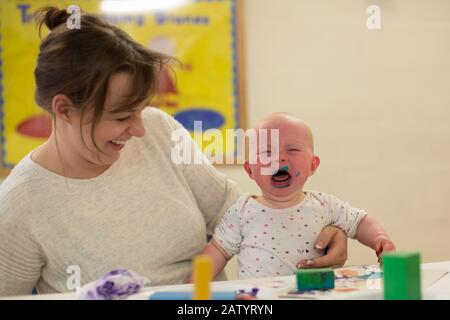 Une jeune maman avec son bébé de 9 mois qui pleure à un groupe de jeu. ROYAUME-UNI Banque D'Images