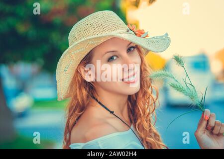 Belle femme confiante à l'extérieur personne heureuse. Tenue d'été jeune fille regardant votre appareil photo émotions humaines positives visage expression tenant herbe. Banque D'Images