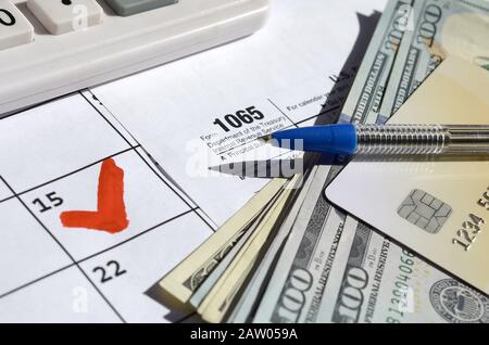 1065 Revenus de la société vide avec des dollars, calculatrice et stylo sur la page calendrier avec marqué le 15 avril. Période fiscale concept. IRS Interna Banque D'Images