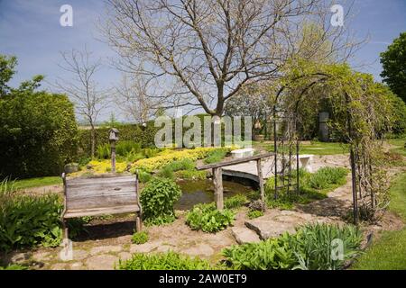 Chemin en pierre de drapeau avec ancien banc de siège en bois et métal noir arbour dans jardin de campagne au printemps Banque D'Images