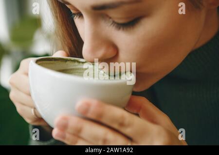 Close-up face ou portrait d'une fille qui boit sain et délicieux thé vert matcha latte Banque D'Images
