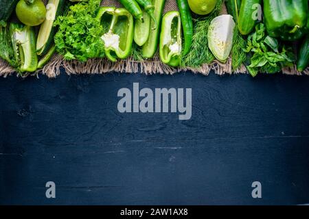 Un grand ensemble de légumes verts disposés sur du tissu de lin, sur un fond en bois. Vue de dessus. Espace libre. Banque D'Images