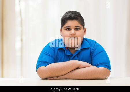 Portrait d'un garçon de chubby assis avec ses mains sur la table. (Obésité) Banque D'Images