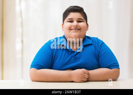 Portrait d'un garçon de chubby assis avec ses mains sur la table. (Obésité) Banque D'Images