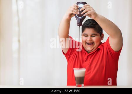 Jeune garçon qui dépose le verre de lait avec du sirop de chocolat.(obésité) Banque D'Images