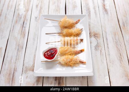 Crevettes croustillantes enveloppées dans la pâte Kataifi appelé aussi Kanafeh, Kadaif. Servi avec de la sauce sur fond blanc vieux bois. Banque D'Images