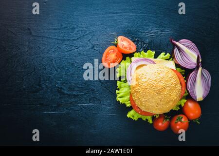 Hamburger au fromage, à la viande, aux tomates, aux oignons et aux herbes. Sur fond en bois. Vue de dessus. Espace libre. Banque D'Images