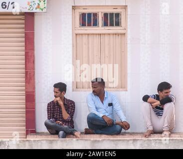 DIU, Inde - décembre 2018: Trois hommes s'assoient sur une étagère à l'extérieur de la fenêtre de fermeture d'un magasin dans les rues de Diu. Banque D'Images