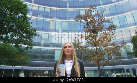 Par en dessous de la blonde woman in suit le café dans la tasse de papier à l'écart sur rue. Banque D'Images