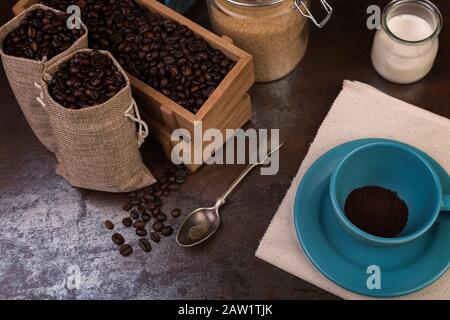 Tasse de sachets de café et de jute, récipients en bois remplis de fèves de cofée sur le fond de rouille. Sucre de canne. Faible luminosité. Banque D'Images